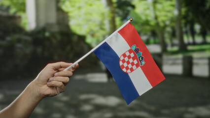 Hand holding croatian flag outdoors in city street with greenery, representing national pride,...