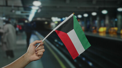 Man holding kuwaiti flag at indoor train station, capturing diverse commuter environment with...