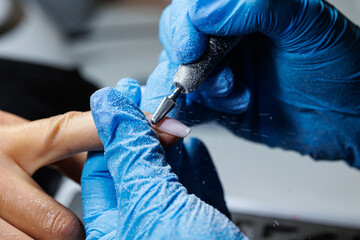 Nail Technician Using Electric File for Manicure, Close-up of nail technician wearing blue gloves using electric nail drill to shape acrylic nails during manicure session.