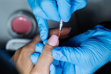 Manicure Process with Nail Brush and Gel Application, Closeup of professional manicurist applying pink gel polish on fingernail using fine brush while wearing blue gloves in salon.