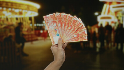 Man holding philippine pesos in hand, set against the lively backdrop of a vibrant outdoor...