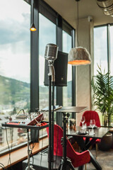 Retro microphone on stand in cozy modern restaurant with mixing console and mountain view through...