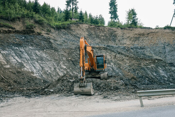 Excavator working at construction site near road. Heavy machinery digging soil on rocky slope with...