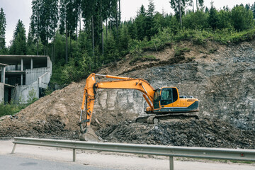 Excavator working at construction site near concrete building structure. Heavy machinery digging on...