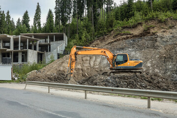 Excavator working at construction site near concrete building structure. Heavy machinery digging on...