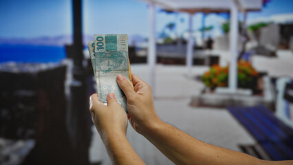 Man holding brazilian reais banknotes outdoors in a summer vacation setting with urban street...
