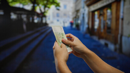 Man counting singapore dollars on a vibrant city street, showcasing hands in focus with blurred...