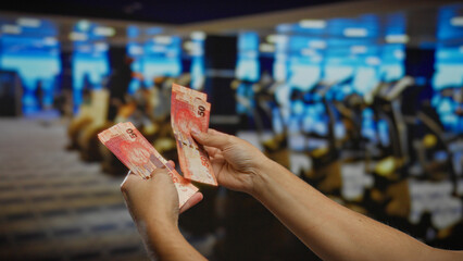 Man holding south african rand indoors at a gym, featuring colorful banknotes and fitness equipment...