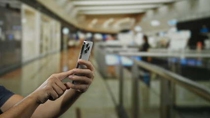 Man holding smartphone in indoor shopping center with blurred background suggesting communication and technology context.