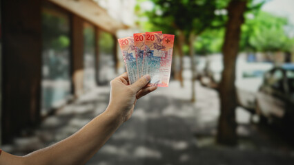 Man holding swiss franc banknotes in his hand on a bustling city street, illustrating urban finance...