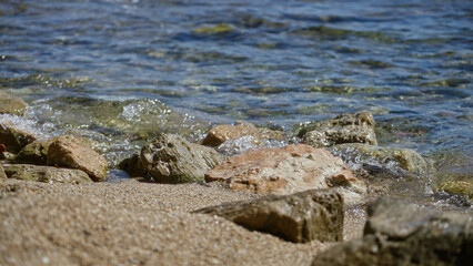 Mediterranean seaside with clear water washing over sunlit stones on a sandy beach under a bright sunny sky capturing the essence of a tranquil outdoor summer day.