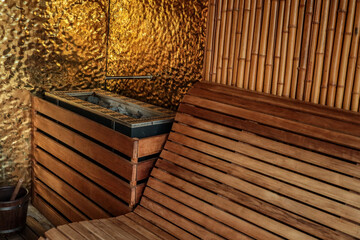 Cozy sauna interior with wooden bench, heater with stones, bamboo wall, and golden textured...
