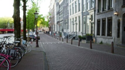 Blurred view of an amsterdam street with defocused bicycles and canal, capturing the serene urban atmosphere and architectural beauty of the netherlands.