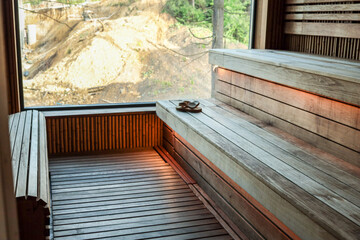 Modern wooden sauna interior with large window overlooking nature. Empty wooden benches, soft lighting and natural design elements create cozy atmosphere for relaxation and wellness