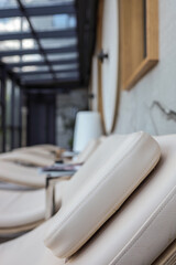 Row of modern spa recliners with soft beige cushions, minimalist side tables and bright natural light through glass walls. Cozy relaxing area in wellness center interior