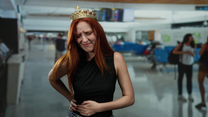 Woman with crown looking distressed at airport terminal suggesting travel discomfort amid crowded indoor setting.