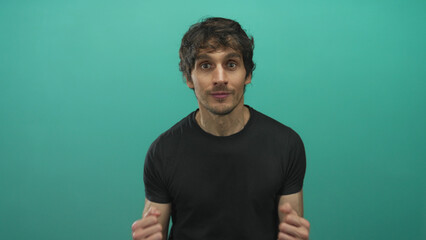 Young man with clenched fists and beaming smile celebrating in studio before a teal wall;...