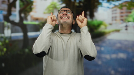Elderly man smiling and pointing upward while standing in a bright urban park setting, highlighting...