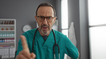 Hispanic man in a hospital clinic wearing a green uniform and stethoscope looks directly into...