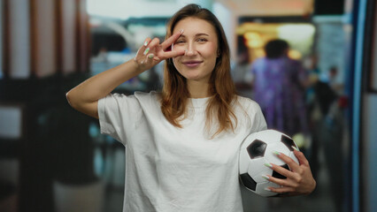 Woman outdoors laughing holding a soccer ball on a busy city street, demonstrating peace sign with...