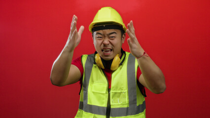 Young man wearing yellow safety vest and hard hat stands confidently against a vibrant red...