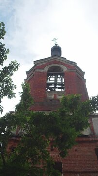 The bell tower of a derelict Orthodox church, constructed of brick, with a lopsided cross at its summit. vertical