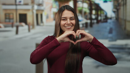 Fototapeta premium Woman making heart gesture on urban street showing happiness and positivity in vibrant setting with attention to youthful feminine energy and outdoor lifestyle.