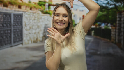 Fototapeta premium Woman smiling with hands framing face on urban street under blue sky showcasing happiness and confidence in a casual outdoor city setting.