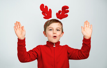Cheerful boy in reindeer antlers on isolated gray background showing different funny emotions,...