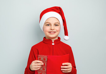 Cheerful boy in Santa hat holding an envelope, postcard, greeting, letter to Santa Claus ,...