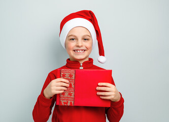 Cheerful boy in Santa hat holding an envelope, postcard, greeting, letter to Santa Claus , surprise, joy, delight. Happy emotions, joy Merry Christmas concept.