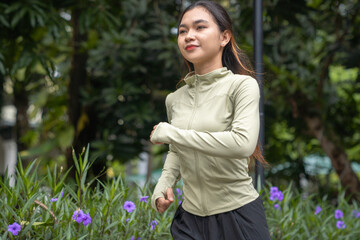 Fit young Asian woman jogging in park smiling happy running and enjoying a healthy outdoor...