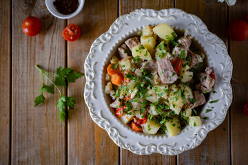 Potatoes with meat on a beautiful white plate on a wooden table. Roast with meat and vegetables for dinner. Close-up
