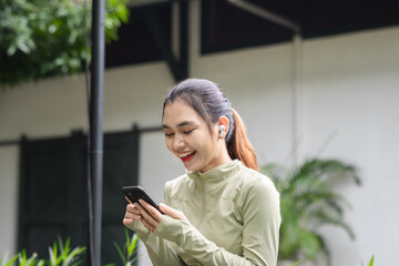 Fit and healthy Asian woman using smart phone after doing exercise in the park. Female jogger....