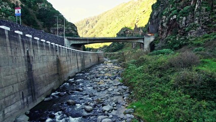 The drone is flying over a mountain river between rocks. It flies under pedestrian bridges