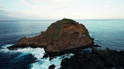Lighthouse on top of a cliff sticking out of the sea. Bird's-eye view. The drone flies up to the lighthouse