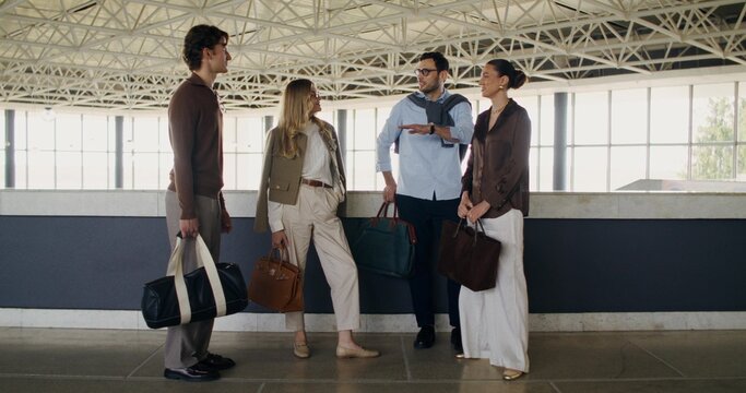 A group of stylish business people are talking and smiling while standing in the airport building
