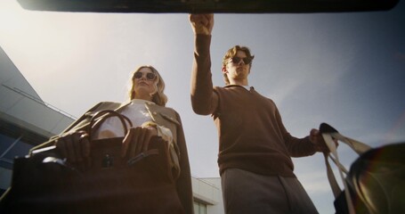 Stylish man and woman put bags in car trunk, view from trunk