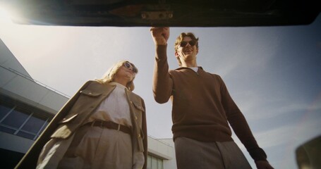 Stylish man and woman take bags out of car trunk, view from trunk
