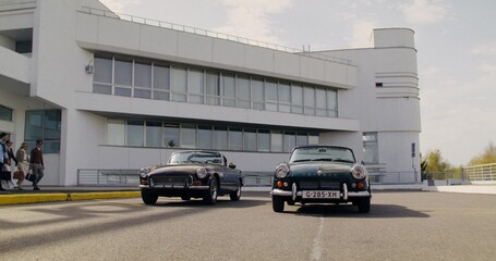 Two young couples put their bags in the trunk of vintage cars on a sunny day