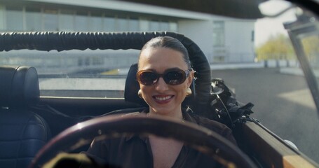 A happy elegant woman starts a retro convertible. A trip on a sunny day. Front view