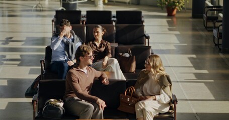 People in the airport or train station waiting room. They're talking in chairs.
