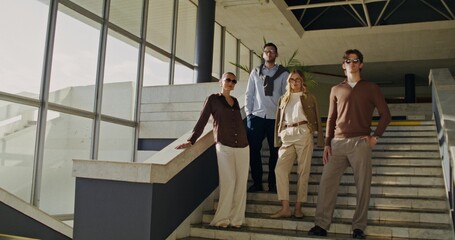 Fototapeta premium A group of stylish young people look at the camera with a serious look standing on the stairs indoors