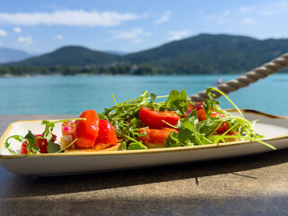 Fresh summer salad with arugula, cherry tomatoes, and feta by a scenic lake view