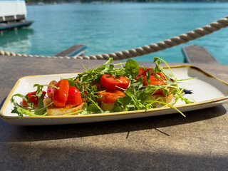 Fresh tomato and arugula bruschetta by lakeside dock on sunny day
