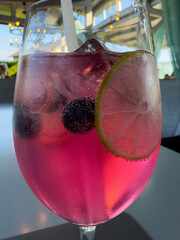 Refreshing pink cocktail with lime and blueberries in a glass with straw