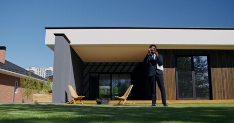 A realtor takes pictures of a house for sale on a mobile phone while standing in the backyard