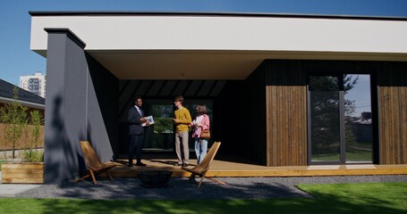 Potential home buyers are talking to a realtor standing on the terrace on a summer day