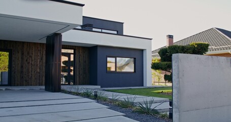 The facade of a stylish minimalist modern cottage with a well-kept house territory on a summer day
