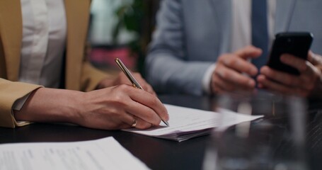 A business man and a woman sign a contract sitting at a desk in an office. Close-up of their hands,...